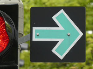 Schild mit grünem Pfeil an roter Ampel